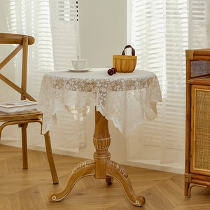 Vintage white lace tablecloth with floral embroidery and scalloped edges on wooden round table