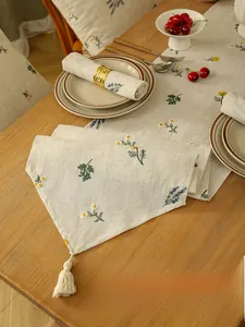 Close-up of linen table runner with floral embroidery and elegant fringe tassel detail
