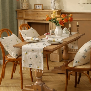 Detail von Leinen-Tischläufer mit floraler Stickerei und Quasten auf einem Holztisch