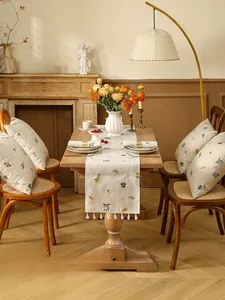 Close-up of pastoral linen table runner with floral embroidery and white fringe details