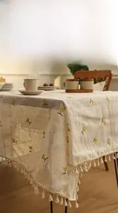 Close-up of linen tablecloth featuring yellow berry embroidery and beige tassel fringe