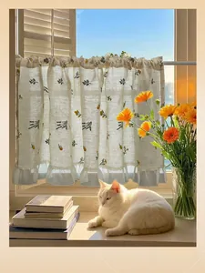 Detail of linen cafe curtain with floral embroidery and white lace trim in natural light