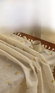 Detailed close-up of linen tablecloth with yellow cherry embroidery and tassel edge