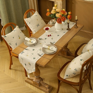 Close-up of pastoral linen table runner with daisy embroidery and white tassels on wood