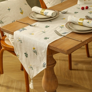 Linen table runner with floral embroidery and white tassels on a solid wood table