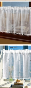 Detail of embroidered cat pattern on white linen cafe curtain with pom-pom trim and seascape