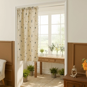 Minimalist beige linen door curtain with floral patterns and tassel trim in sunlight