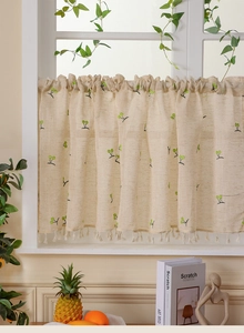 Close-up of beige linen cafe curtain with green embroidery and tassel trim details