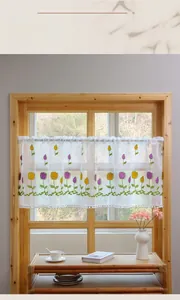 Detail of embroidered yellow tulip lace cafe curtain with decorative white pom-poms