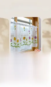 Detail of embroidered tulip lace cafe curtain with pom-poms on semi-sheer white mesh fabric