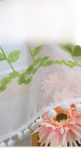Detail of white lace cafe curtain featuring green leaf embroidery and pom-pom trim