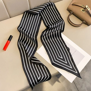 Minimalist black and white striped long silk scarf displayed on a beige leather texture