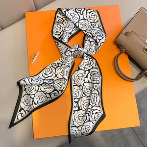 Elegante foulard twilly in seta a fiori camelia bianco e nero annodato su sfondo arancio
