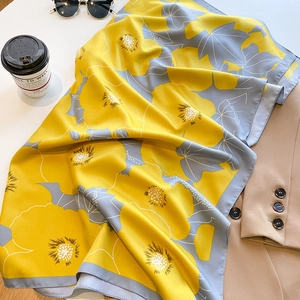 Close-up of yellow floral silk scarf draped over a khaki blazer with stylish accessories