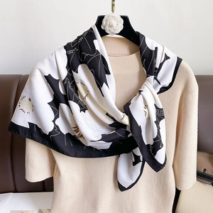 Detailed view of a silk scarf with camellia floral print styled on a beige sweater