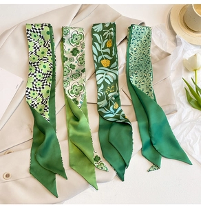 Detailansicht von vier grünen Seidenschals mit Blumenmuster auf einem beigen Blazer