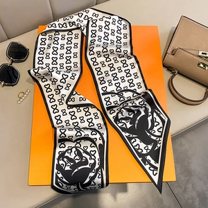 Close-up of black and white bow print silk scarf on orange gift box with accessories