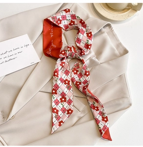 Détail d'un foulard étroit en soie à fleurs rouges noué sur un blazer beige