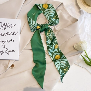 Grüner Satin-Schal mit Blumenmuster als Schleife auf einem beigen Blazer professionell drapiert