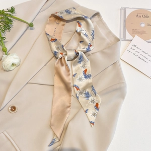 Elegant champagne silk skinny scarf with floral print tied on a beige blazer lapel