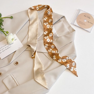 Detail of floral silk twilly scarf draped on a beige blazer with elegant floral props