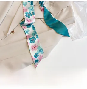 Detail eines schmalen Seidenschals mit Blumenmuster auf einem beigen Blazer
