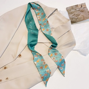 Details eines blaugrünen Seidenschals mit Blumenmuster auf einem beigen Blazer