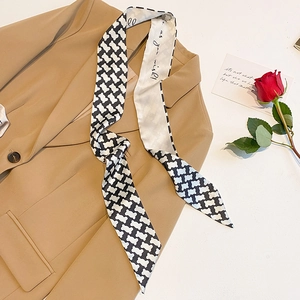 Detail of black and white geometric silk scarf draped on a beige blazer with red rose