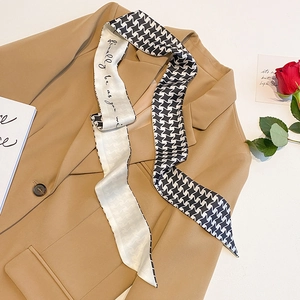 Detail of a houndstooth and script print twilly scarf draped on a camel blazer