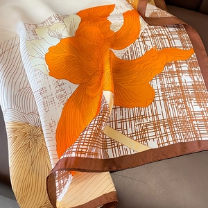Detail of silk scarf with orange floral pattern and geometric grid on leather background