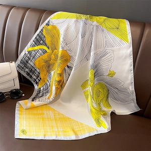 Elegant floral silk scarf in yellow and black draped on a stylish brown leather sofa