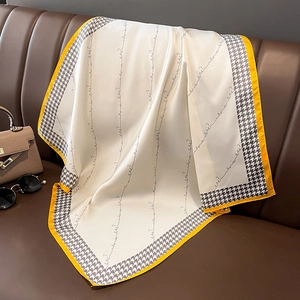 Eleganter Seidenschal mit Hahnentrittmuster und gelbem Rand auf braunem Lederhintergrund