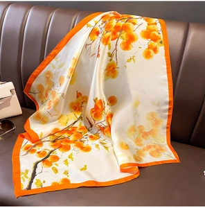 Detail of square silk scarf with persimmon pattern draped on a leather couch