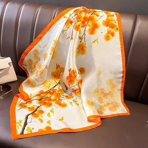 Silk-feel scarf with persimmon print and orange edges on a brown leather sofa