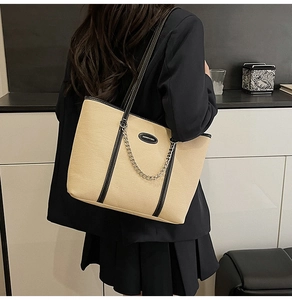 Dettaglio di una borsa tote in tessuto beige con finiture in pelle nera e catena argento