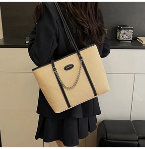Dettaglio della borsa tote beige con bordo nero e catena in metallo su modella in abito