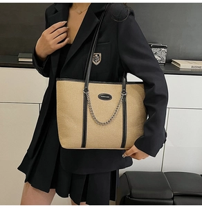 Dettaglio della borsa tote in tela con finiture in pelle nera e catena su outfit da lavoro