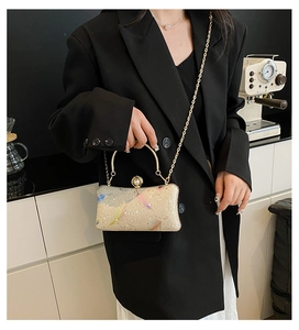 Bolso de noche champán con plumas de colores y cadena dorada sostenido por una modelo