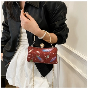 Detalle de bolso de fiesta rojo brillante con estampado de plumas y cierre de perla