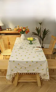 Detailed view of beige tablecloth featuring yellow floral embroidery and white fringe tassels