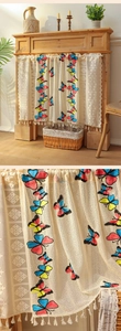 Detailed embroidery of colorful butterflies on a cream lace cafe curtain with tassels