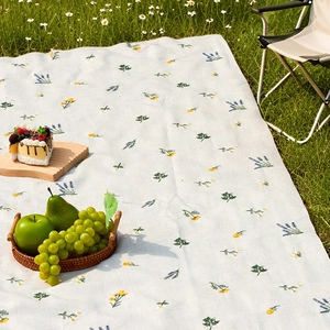 Outdoor picnic mat with floral embroidery on green grass with picnic basket and accessories
