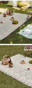 Detail of grey floral print and wide hollow lace border on a beige outdoor picnic mat