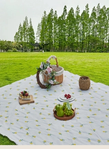 Detail showing high-quality waterproof picnic mat with yellow floral print on green lawn