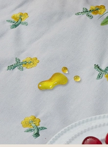 Detail of waterproof picnic mat showing liquid beading on yellow floral embroidery fabric