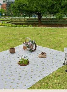 Close-up of waterproof picnic mat with yellow floral pattern and fringe on green grass