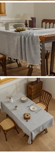 Detailed view of gray linen tablecloth with white tassels on a wooden dining table