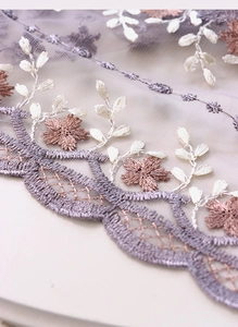 Gros plan sur nappe en dentelle lilas avec broderie florale blanche délicate