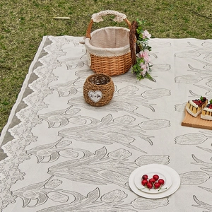 Outdoor picnic mat with grey tulip print and lace edges on green grass with picnic basket