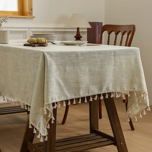 Thick light green linen tablecloth with tassels on a rustic wooden dining table
